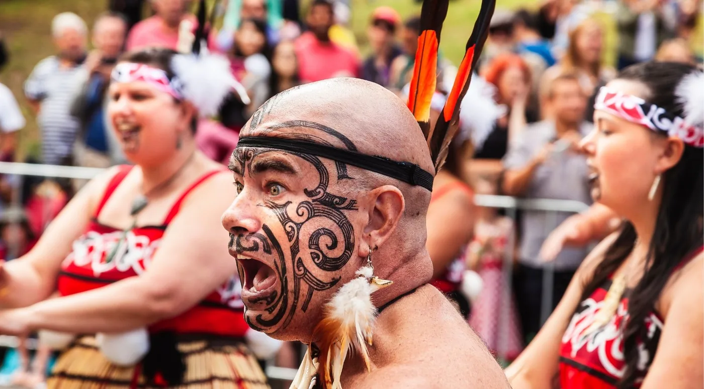 Kapa haka performers in feathered headbands and korowai performing a haka before an audience