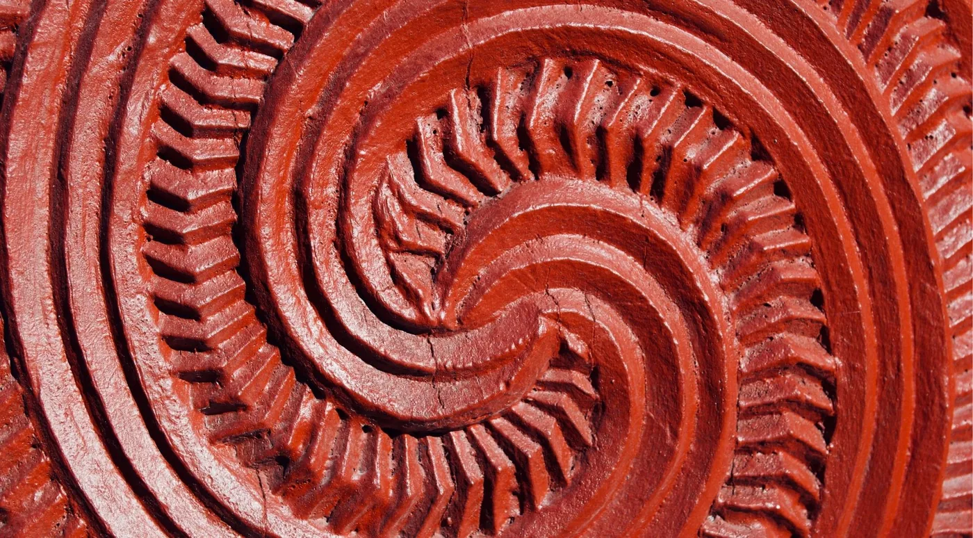Close-up of a kōkōwai red-ochre carved spiral in wood, showing chisel texture