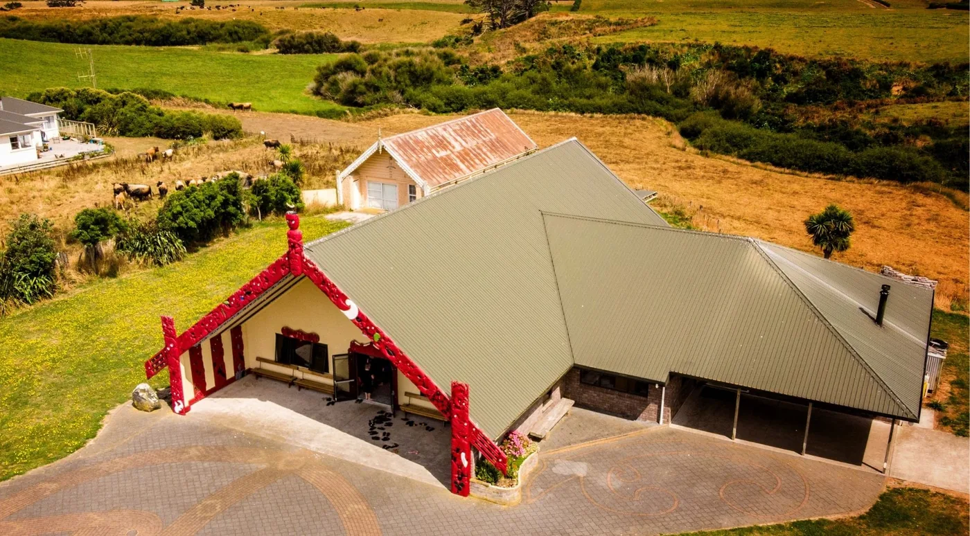 Aerial view of a carved red wharenui meeting house on a marae surrounded by green farmland